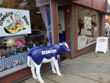Image shows the Wooden Shoe store front. In front of the store is a statue of a blue Beemster cow.