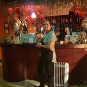 The restaurant owners wife Asmeret stands in front of the counter with the grass canopy and "Blue Nile" sign, a collection of traditional East African arts and artifacts decorates the counter